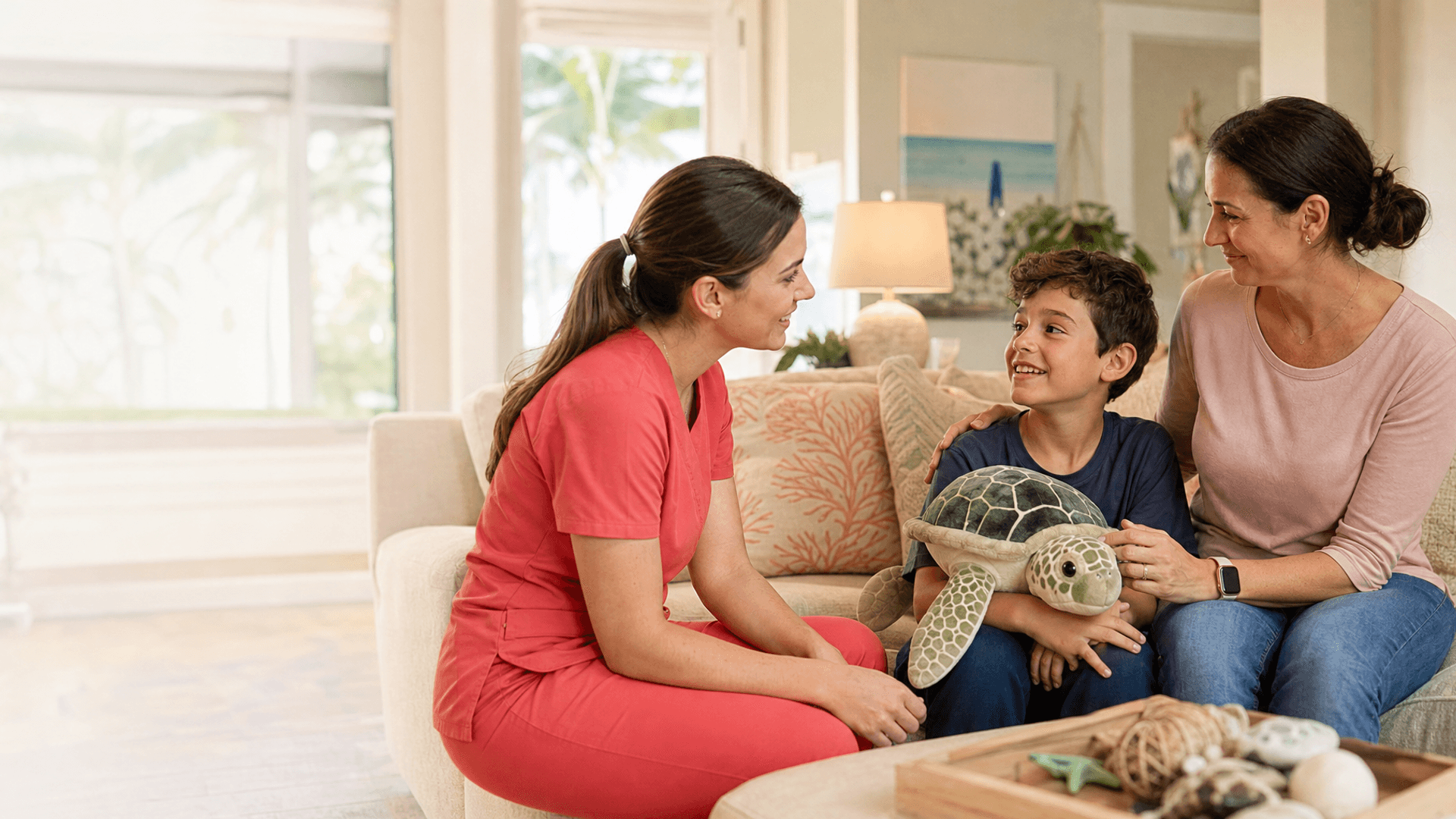 Pediatric hospice nurse in plain coral scrubs supporting a child and parent at home